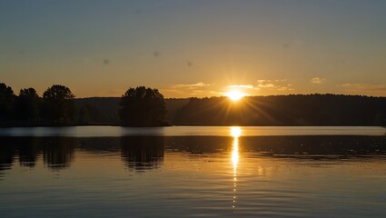 Obraz premium image shows a sunset over a lake. The sun is setting behind a hill,