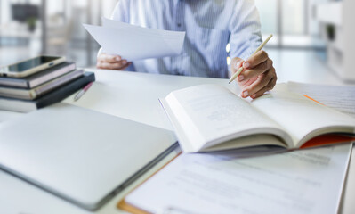 Asian businessman working in office holding business report and find information about a business in a book