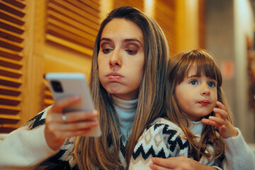 Mom Checking her Smartphone While Holding her daughter in Restaurant. Distracted mom being...