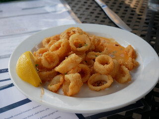 Fried calamari squid appetizer on white plate, on outdoor black table. Delicious seafood lunch.