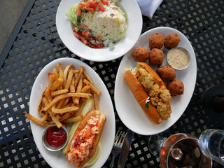 Seafood lunch table setting with different delicious food outdoors, top view. Wedge caesar salad, shrimp po boy sandwich with fries, hush puppies, and lobster roll sandwich.