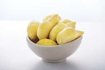 Ripe yellow durian peeled in a white cup, on a white background.