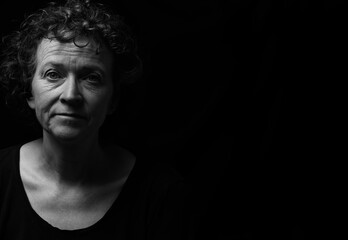 Black and white portrait of a middle aged woman with curly hair. Off center, room for copy. 