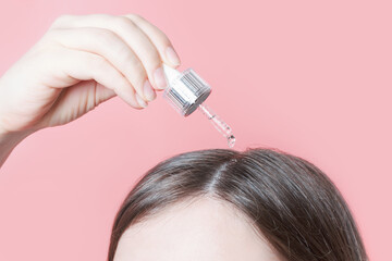 Young woman applying oil to her hair with a pipette on a pink background close-up.