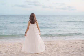 Happy traveler woman in white dress enjoy beautiful sea view, young woman standing on sand and...