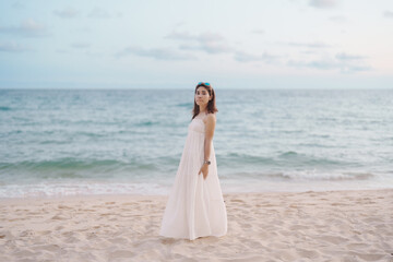 Happy traveler woman in white dress enjoy beautiful sea view, young woman standing on sand and looking ocean at tropical beach. Freedom, relaxing, vacation holiday and summer travel concept
