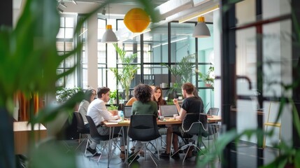Blurred photo of diverse coworkers sitting around table in modern office space with plants. AIG535