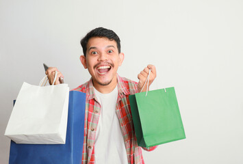 portrait of happy smiling handsome Asian man carrying shopping bags and his smartphone. Online shop...
