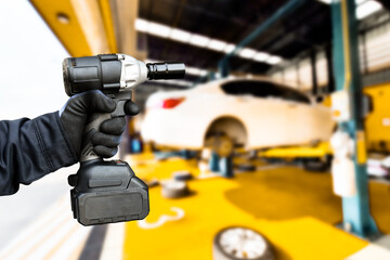 Car repair and maintenance servicing concept , Hand of an auto mechanic using a cordless impact wrench in a car repair facility center