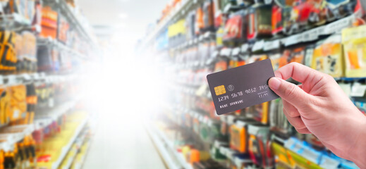 Hand holding a debit card or credit card in order to make a payment , shopping mall blurred on background with copy space for text , Credit or debit card and financial concept