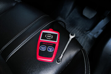 OBD2 or OBD scanner and wrench on car leather seat for engine system analysis to fixing car engine...