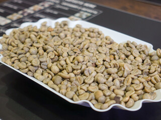 Fresh coffee beans in a white plate placed on the table