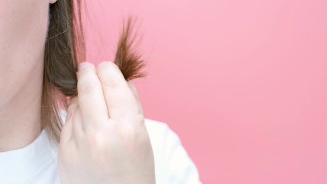 Woman holding her hair with split ends close-up on pink background.