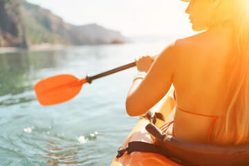 woman bikini paddles kayak on a lake. The sun is shining brightly, creating a warm and inviting...