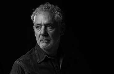 Low key black and white portrait of an attractive older Caucasian man with grey hair and beard. Looking to the right with serious or pensive expression.  Room for copy.
