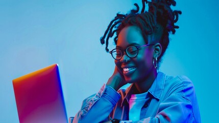Young lgbtq+ African Woman Smiling While Using Laptop in Neon Blue and Pink Lighting, Wearing Glasses and Denim Jacket, Enjoying Creative Work or Online Study
