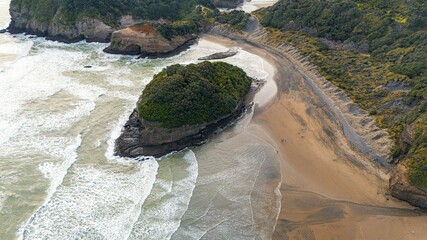 A dramatic aerial view of coastal cliffs with rolling waves crashing against the rocky shore, under...