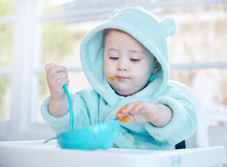 Baby, eating and mess in feeding chair with food, learning and spoon for health, nutrition and care...