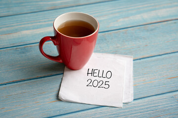 Hello 2025, typed words on white paper napkin next to cup of coffee.
