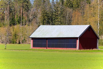Solar panels installed on the exterior wall of a red barn in rural area on a sunny day of spring.