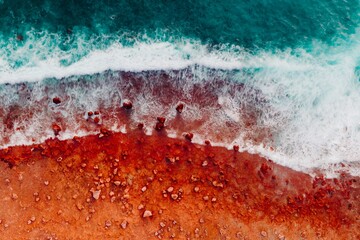 Aerial View of Turquoise Blue Ocean Beach With Crashing Waves and Red Dirt Sand and Rocks