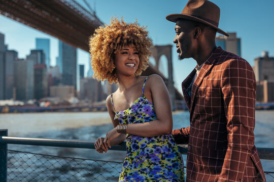 Couple smiling and talking to each other next to a metal fence - Powered by Adobe