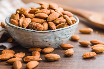 Peeled almond nuts in bowl on wooden table.