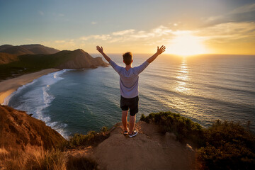 Man with arms raised in the air, celebrating success and achievement, standing on cliffs overlooking the ocean at sunset. 