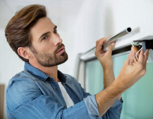 handsome worker man installing home window curtain rod on the wall windows house