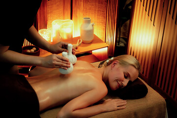 Hot herbal ball spa massage body treatment, masseur gently compresses herb bag on woman body....