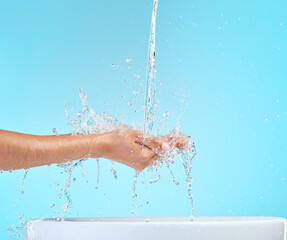 Fototapeta premium Person, hands and water splash with sink for hydration, cleaning or hygiene on a blue studio background. Closeup of liquid droplets, aqua or natural mineral for washing, cleanse or droplets in basin
