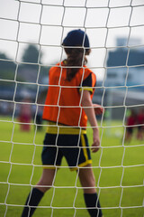 Close up football goal net, seeing a young girl soccer goalkeeper watching her teammates playing. Youth Soccer game on a sunny summer school tournament Day. A football match going on in a background. © athichoke.pim