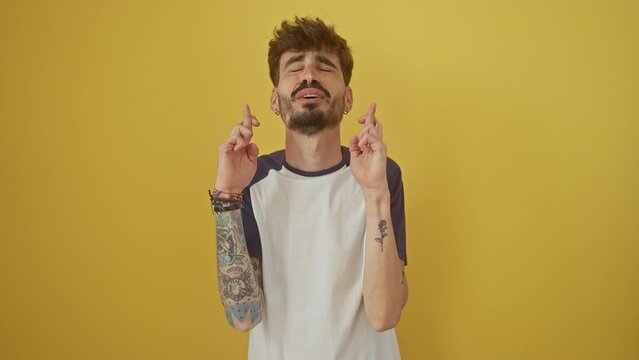 Young hispanic man standing with fingers crossed for luck, eyes closed with hope, making a superstitious gesture on an isolated yellow background