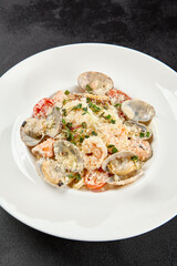 Seafood pasta with vongole, clams, salmon fish and prawns in white plate. Spaghetti marinara with seafood and cheese on dark background. Seafood menu -  pasta in mediterrian  style on black table.