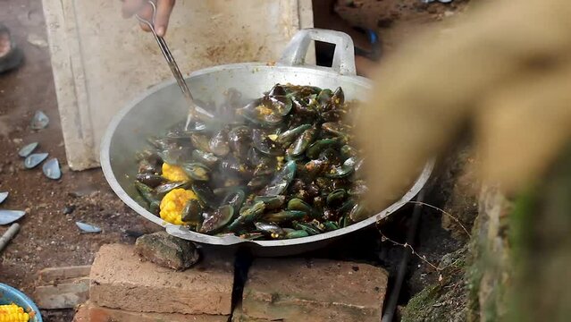 the process of cooking green mussels or Perna viridis, mixed with corn and spicy stir-fry spices.