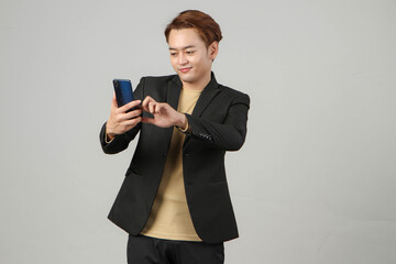 portrait of happy asian businessman wearing suit holding mobile phone on isolated background