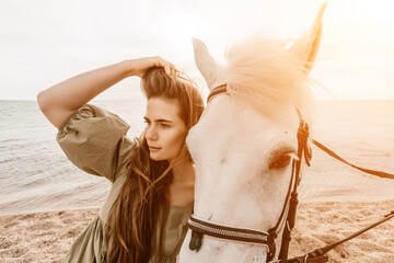 A woman in a dress stands next to a white horse on a beach, with the blue sky and sea in the...