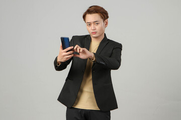 portrait of pensive thoughtful asian businessman wearing suit holding mobile phone on isolated...
