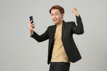 portrait of happy asian businessman wearing suit holding mobile phone with clenched fist...