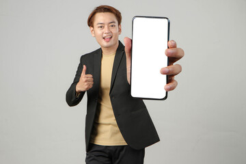 portrait of happy asian businessman wearing suit holding mobile phone and showing blank screen  on...
