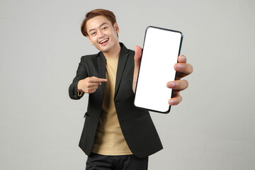 portrait of happy asian businessman wearing suit holding mobile phone and showing blank screen ...