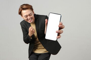 portrait of happy asian businessman wearing suit holding mobile phone and showing blank screen  on...