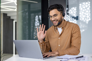 Smiling man in a headset waving during an online video call in a modern office