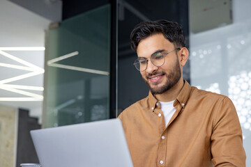 Smiling young man in a modern office working on a laptop