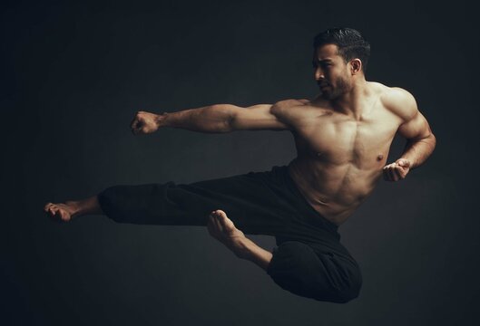 Martial arts, kick and man in jump, motion and fitness for wellbeing in studio backdrop for karate or capoeira. Male person, foot and taekwondo in black background for sports, wellness or workout
