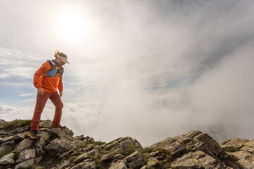 A man in an orange jacket stands on a rocky mountain top