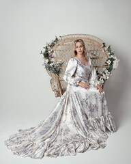 portrait of beautiful blonde female model wearing romantic historical white bridal gown. sitting...