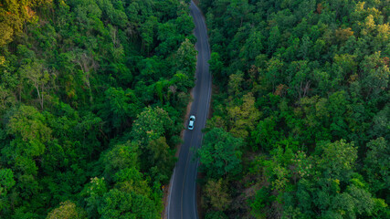 Aerial view of dark green forest road and white electric car Natural landscape and elevated roads...