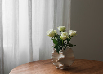 White roses in a ceramic creative vase on a round wooden table in the living room