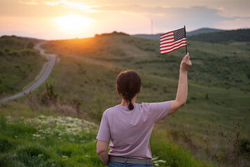 Woma holding a waving american USA flag outdoor in the sunset.